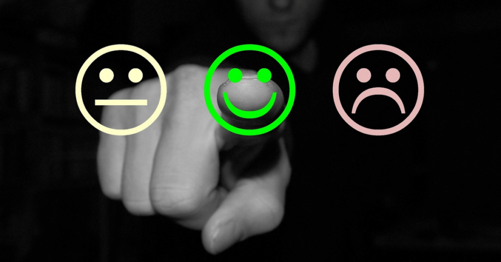 drei Smileys: einer lachend, einer neutral und einer unglücklich vor schwarzem Hintergrund, mit Faust in schwarzweiß